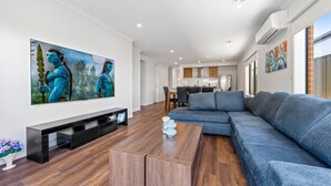 A modern living room with a large flat-screen TV, a grey sectional sofa, and a wooden coffee table. - New Luxury Home • Perfect for Families & WorkStays (Mickleham)