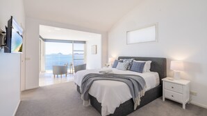 A modern bedroom with a large bed, a bedside table with a lamp, and a view of the sea through a glass door. - Wanda Beach Waterfront , 161 Soldiers Point Rd - waterfront, air con, linen, Wi-Fi (Salamander Bay)