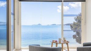 A room with a large sliding glass door leading to a balcony with a view of the sea and distant islands. There is a small round table with a plate of food and a cup on it. - Wanda Beach Waterfront , 161 Soldiers Point Rd - waterfront, air con, linen, Wi-Fi (Salamander Bay)