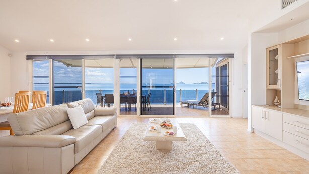 A modern living room with a large sliding glass door leading to a balcony with a sea view. - Wanda Beach Waterfront , 161 Soldiers Point Rd - waterfront, air con, linen, Wi-Fi (Salamander Bay)