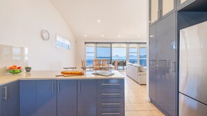 A modern kitchen with a large island, dark cabinets, and a view of the sea through large windows. - Wanda Beach Waterfront , 161 Soldiers Point Rd - waterfront, air con, linen, Wi-Fi (Salamander Bay)