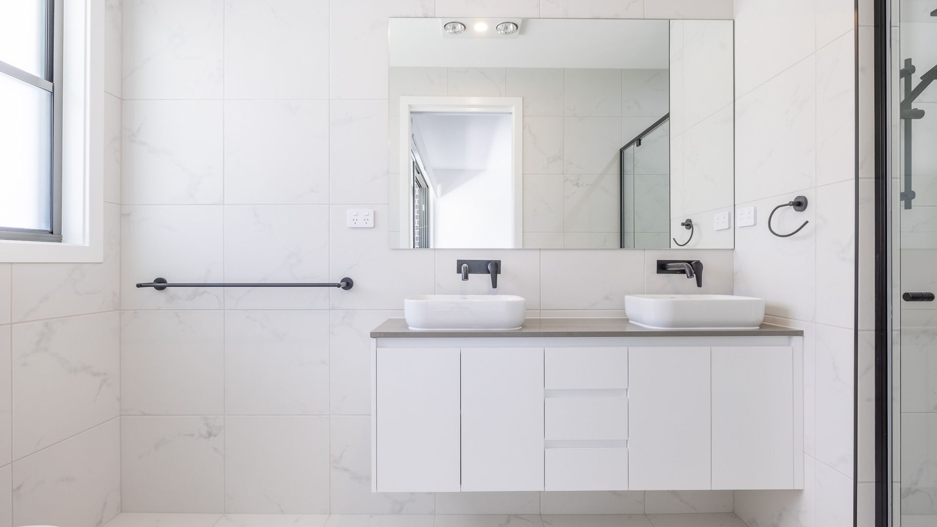 A modern bathroom with two sinks, a large mirror, and a glass shower enclosure.