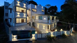 Une maison moderne à deux étages, dotée d’un balcon et de nombreuses fenêtres, entourée d’arbres.