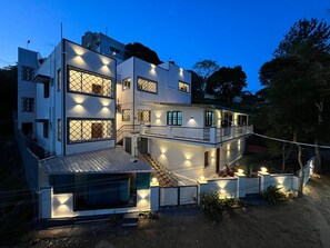 Une maison moderne à deux étages, dotée d’un balcon et de nombreuses fenêtres, entourée d’arbres.