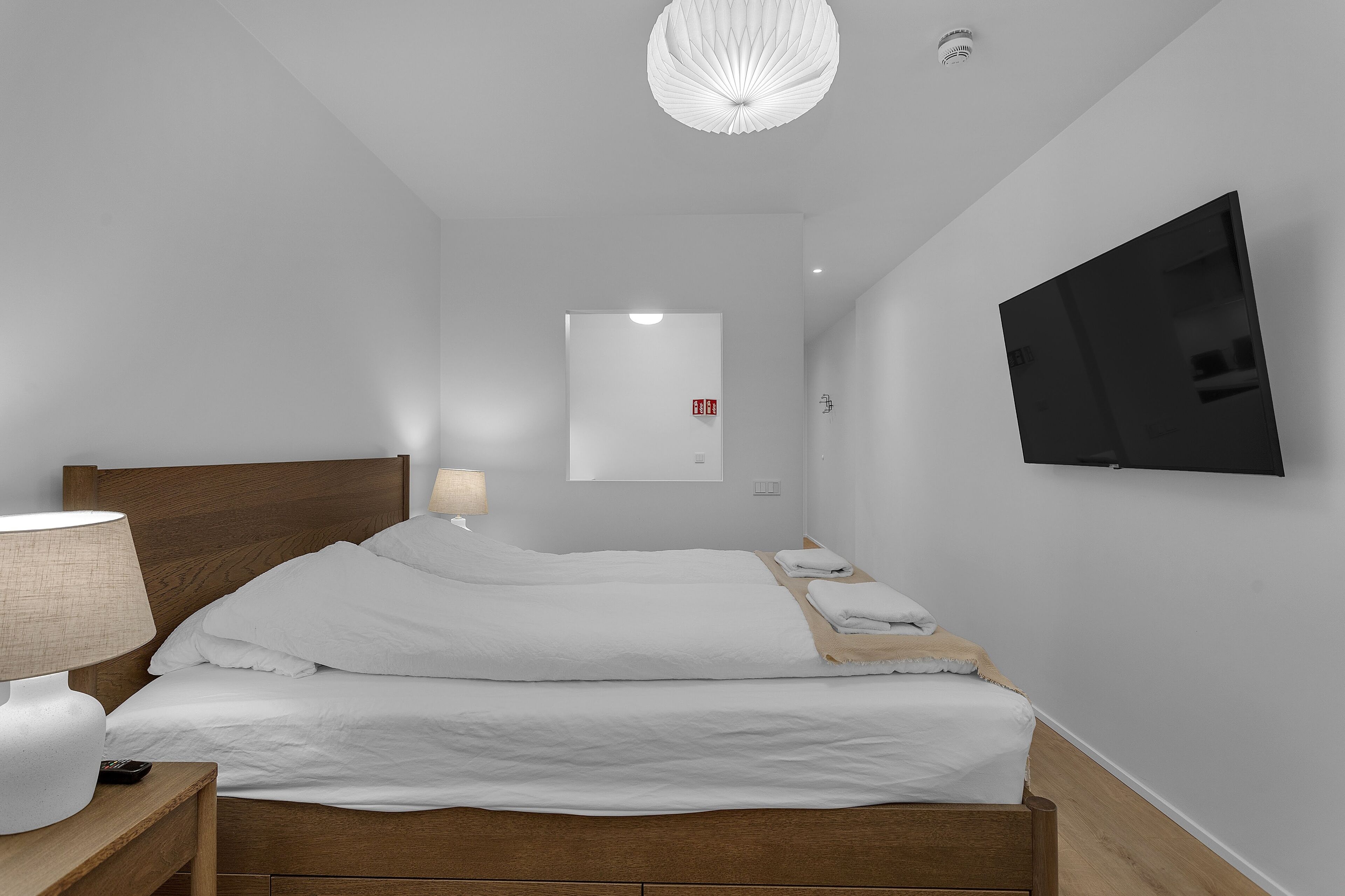 Een moderne hotelkamer met een groot bed, een nachtkastje met een lamp, een flatscreen televisie aan de muur en een plafondlamp.
