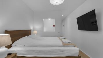 Een moderne hotelkamer met een groot bed, een nachtkastje met een lamp, een flatscreen televisie aan de muur en een plafondlamp.