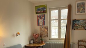 A bedroom with a large bed, a small table with flowers, a chair, and a window with curtains. - Bucolic apartment - Historic heart of Dijon (Dijon)