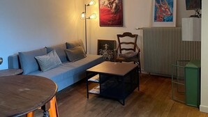 A cozy living room with a sofa, a wooden coffee table, a dining table with chairs, and a radiator. - Bucolic apartment - Historic heart of Dijon (Dijon)