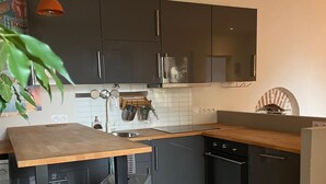 A modern kitchen with dark cabinets, a wooden countertop, and a built-in oven. There are two stools, one pink and one blue, and a hanging orange pendant light. - Bucolic apartment - Historic heart of Dijon (Dijon)