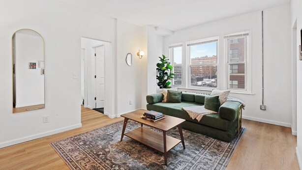 A living room with a green sofa, a wooden coffee table, a patterned rug, and a large mirror. - Luxury Lofts | Minutes From Downtown (Detroit)