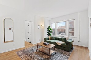 A living room with a green sofa, a wooden coffee table, a patterned rug, and a large mirror.