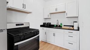 A modern kitchen with white cabinets, a black stove, and a black countertop. - Luxury Lofts | Minutes From Downtown (Detroit)