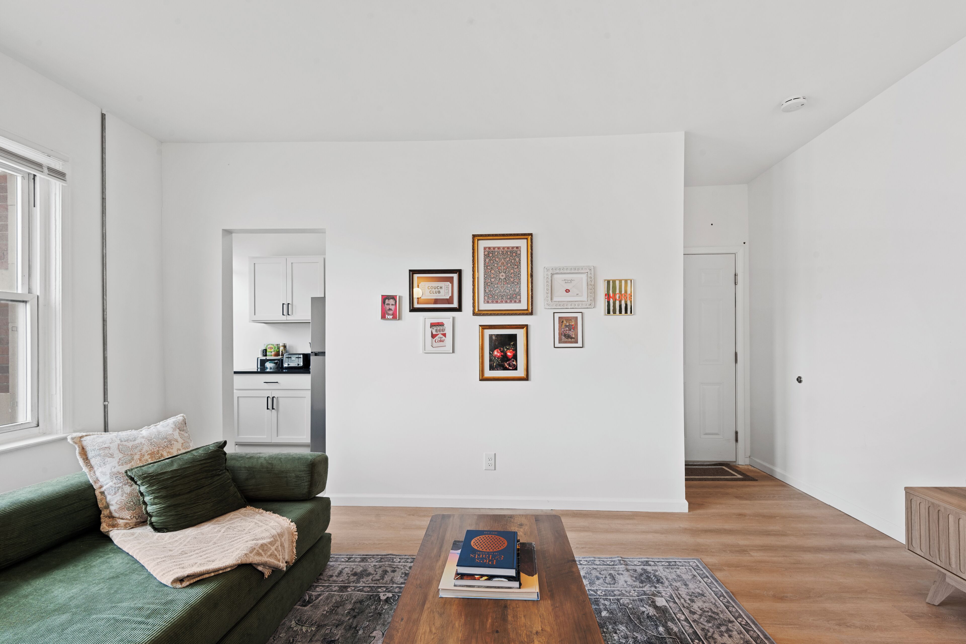 Ein Wohnzimmer mit einem grünen Sofa, einem Couchtisch mit Büchern und einer Wand mit gerahmten Bildern.