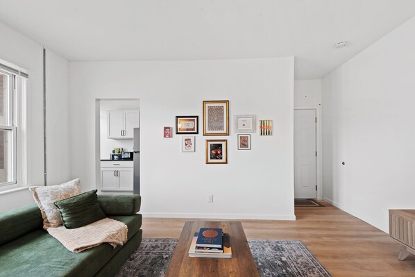 A living room with a green sofa, a coffee table with books, and a wall with framed pictures.