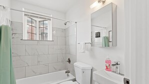A modern bathroom with a bathtub, toilet, and a shower area. - Luxury Lofts | Minutes From Downtown (Detroit)