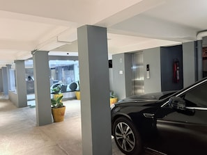 A parking garage with concrete pillars, a black car, and a fire extinguisher. - The Base Inn (Vanur)