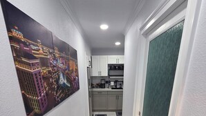 A narrow hallway with a cityscape painting on the left, a kitchen area in the background, and a green door on the right. - Comfort, location and a fair price, ALL IN ONE PLACE (Las Vegas)