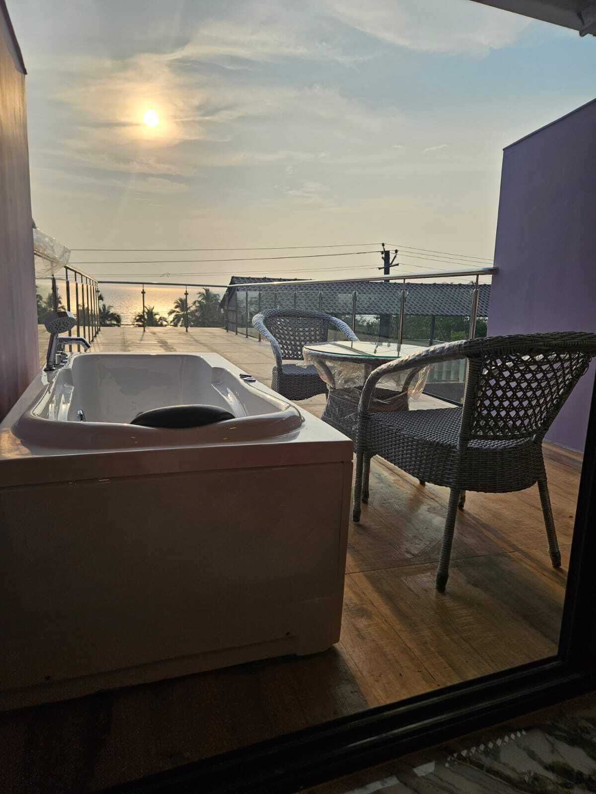 A balcony with a hot tub, wicker chairs, and a view of the sea during sunset.