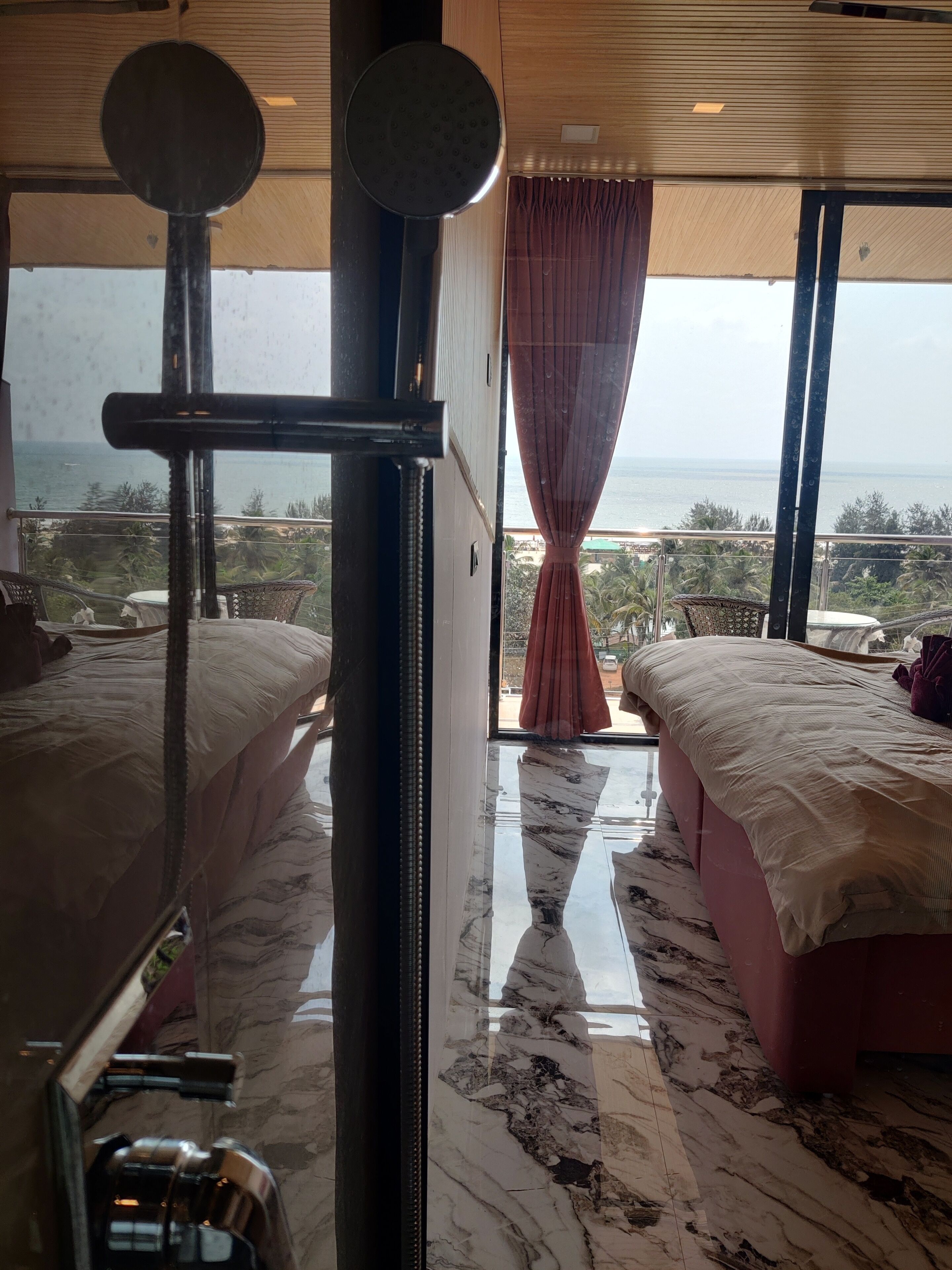A bedroom with two beds, a large window with a view of the sea, and a curtain.
