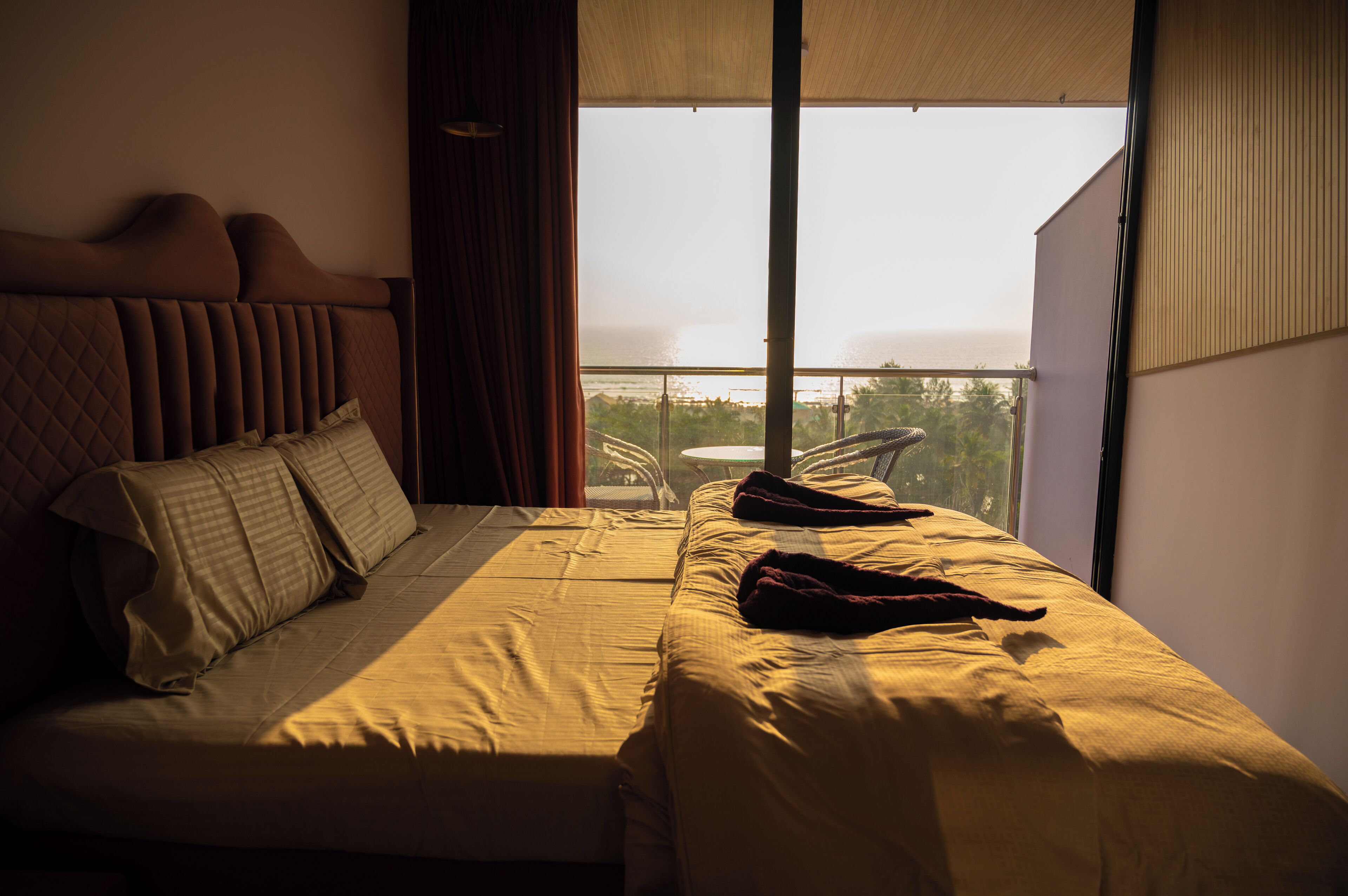 A hotel room with a large bed, a view of the ocean, and a balcony with a table and chairs.