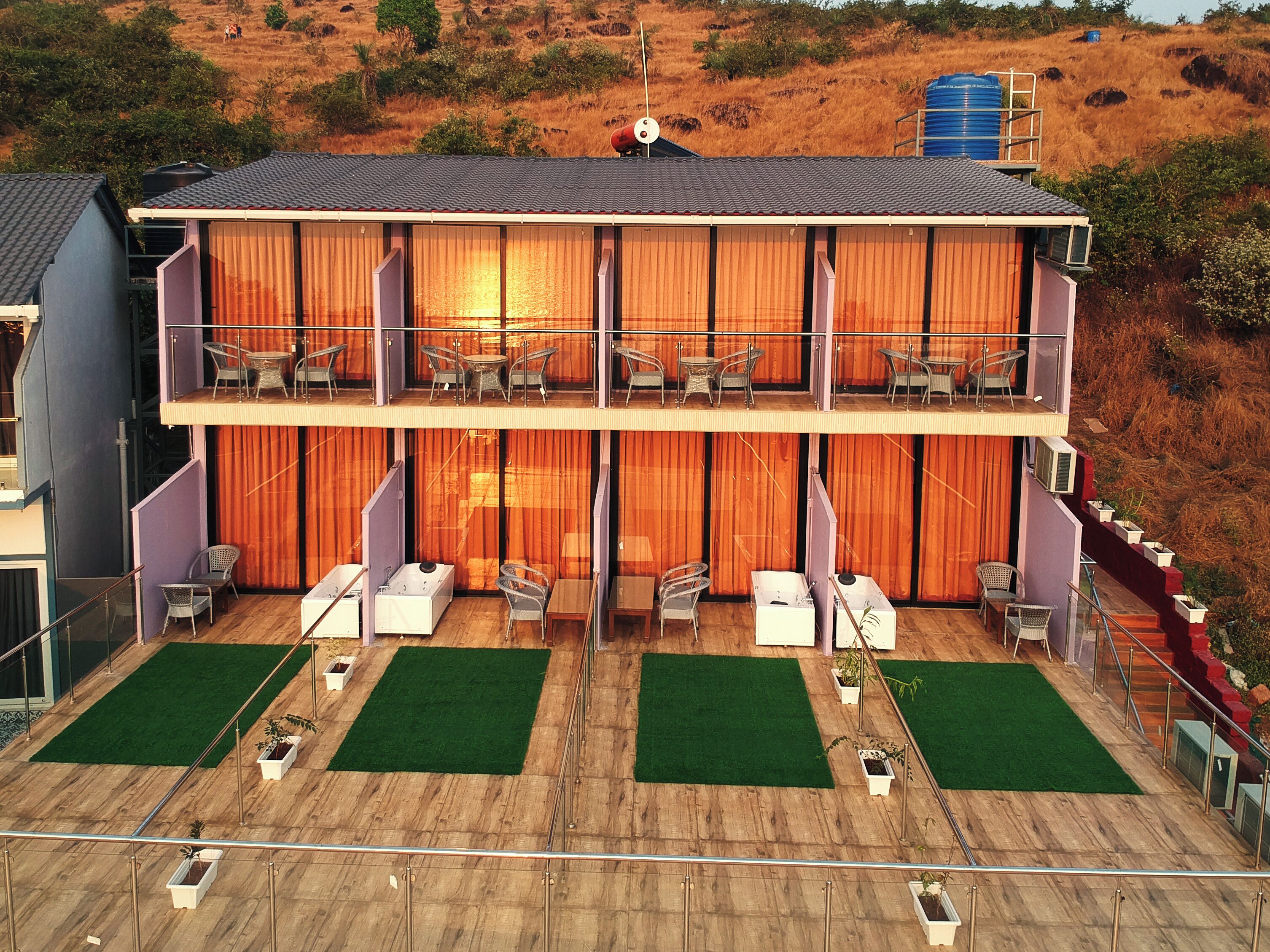 A two-story building with a balcony on each floor, furnished with chairs and tables, and a green lawn area.