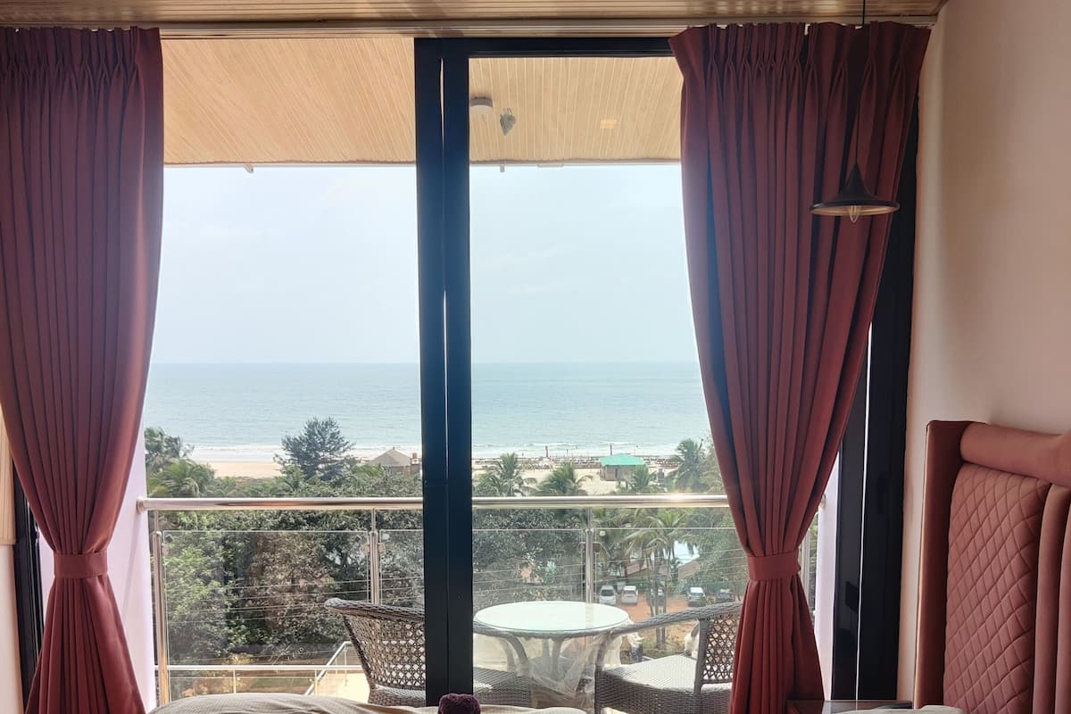 A hotel room with a large bed, a balcony with a view of the beach, and a table with chairs outside.