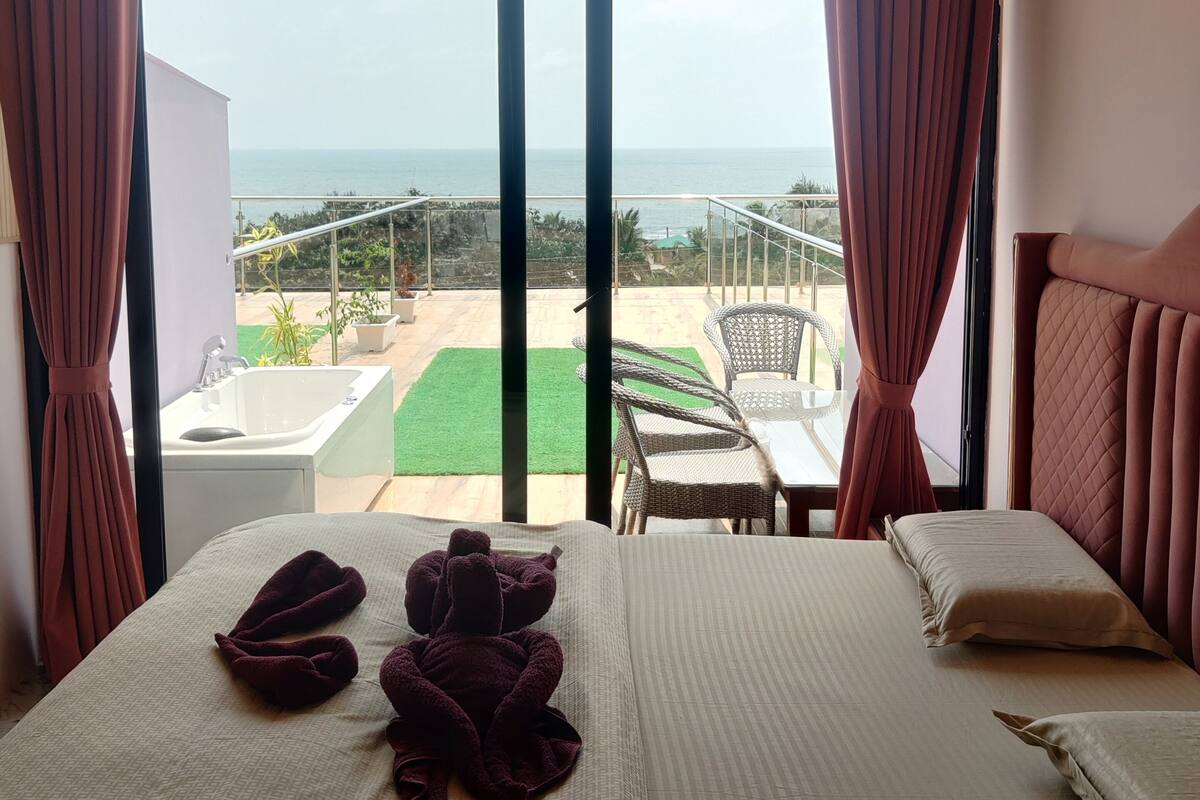A hotel room with a bed, a view of the sea, and a balcony with outdoor furniture.