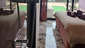 Camera d'albergo con due letti, una ventola a soffitto, vista sulla spiaggia e un'ampia finestra.