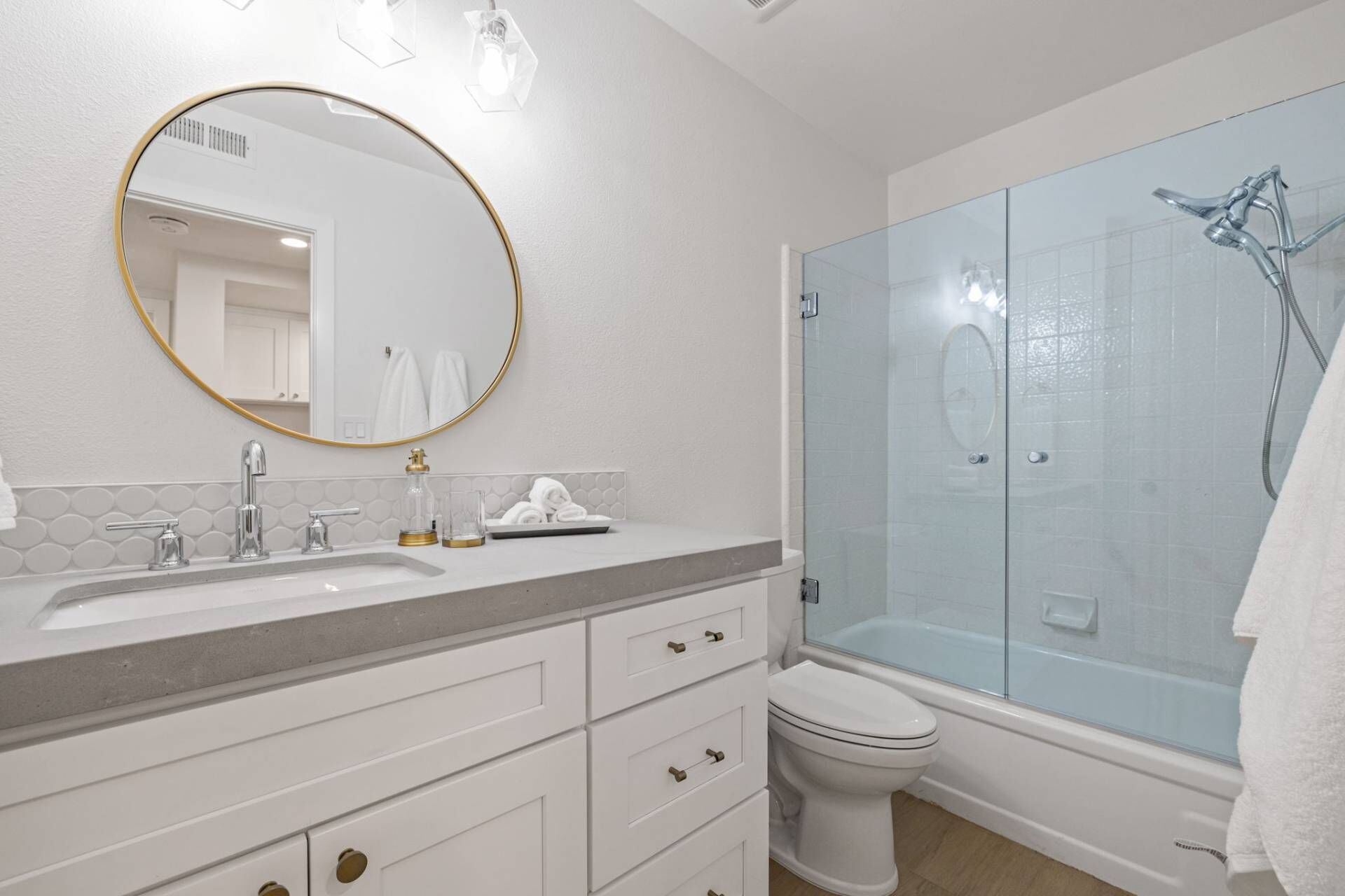 A modern bathroom with a large mirror, a sink with two faucets, a toilet, and a glass-enclosed shower.