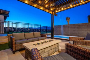 An outdoor patio with a stone fire pit, wicker furniture, and a view of a mountainous landscape.