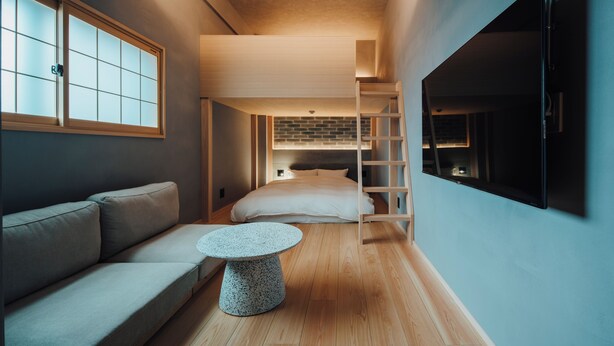 A compact bedroom with a bed, a wooden ladder, a TV, and a small round table. - muku irifune (Kure)