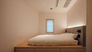 A minimalist bedroom with a built-in bed, a small window, and a wall-mounted light fixture. - muku irifune (Kure)