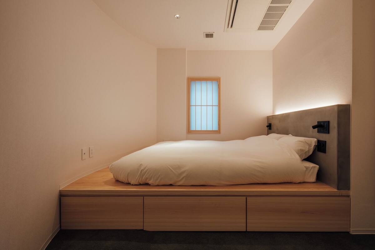 A minimalist bedroom with a built-in bed, a small window, and a wall-mounted light fixture.