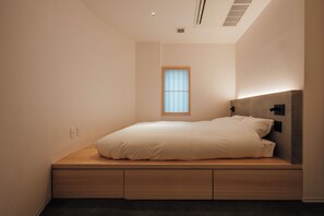 Un dormitorio minimalista con una cama empotrada, un ventanal pequeño y un aplique de pared.