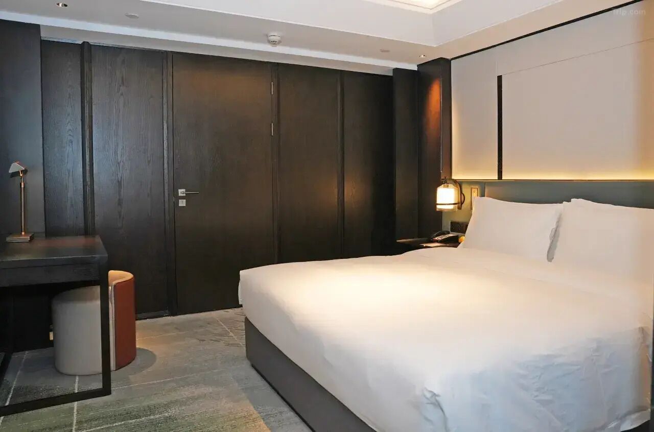 Une chambre d’hôtel avec un grand lit, un bureau, une chaise, une armoire et une table de chevet avec une lampe.