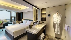 A modern hotel room with a large bed, a separate bathroom with a mirror, and a view of the city. - CANTON HOTEL BEIJING (Beijing)
