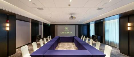 A conference room with a long table, white chairs, and a projector screen.