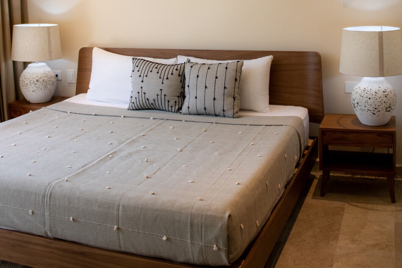 A neatly made bed with a grey duvet, two pillows, and a bedside table with a lamp.