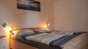 Un lit simple avec une tête de lit en bois, une table de chevet avec une lampe et un tableau accroché au mur.