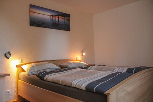 A single bed with a wooden headboard, a nightstand with a lamp, and a painting on the wall.