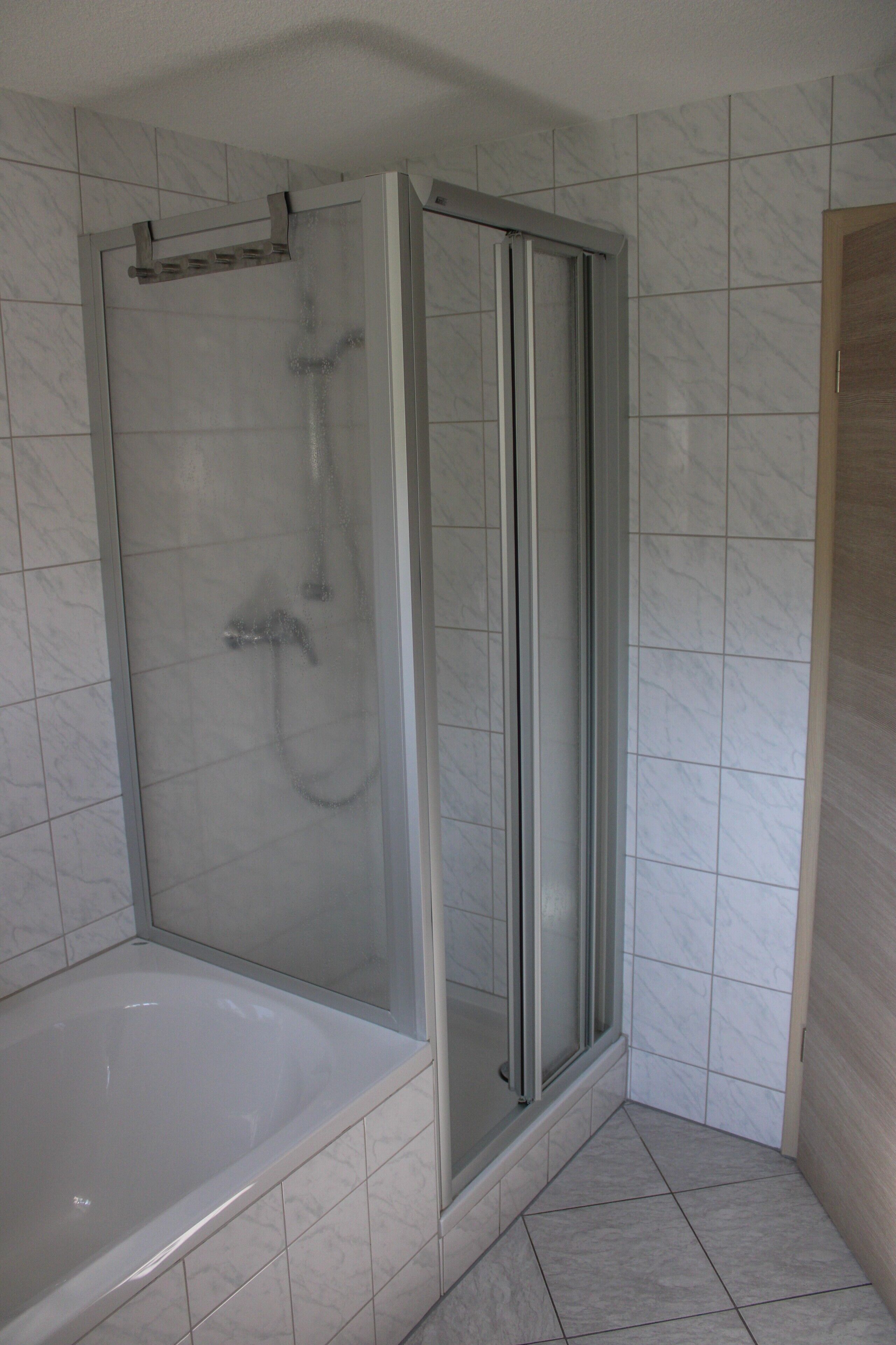 A bathroom with a glass-enclosed shower, a bathtub, and tiled walls.