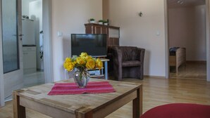 Un salon avec une table en bois, un téléviseur, un fauteuil marron et un vase rempli de fleurs jaunes.
