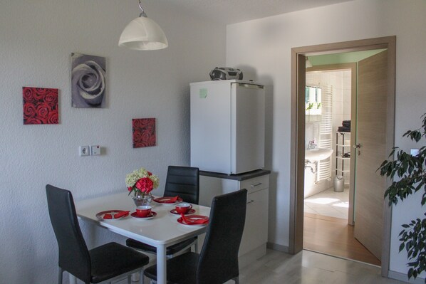 A dining area with a white table, black chairs, and red tableware. There is a white refrigerator and a white cabinet in the background.