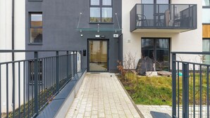 En modern byggnad med en entré av glas, en balkong med utemöbler och en stenlagd gångväg.