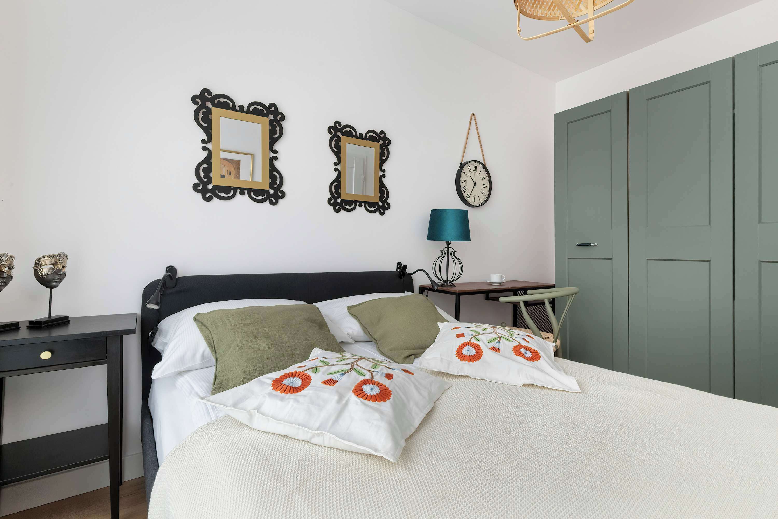 A neatly arranged bedroom with a bed, bedside table, lamp, and two wall mirrors.