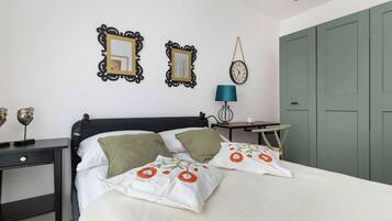 A neatly arranged bedroom with a bed, bedside table, lamp, and two wall mirrors.