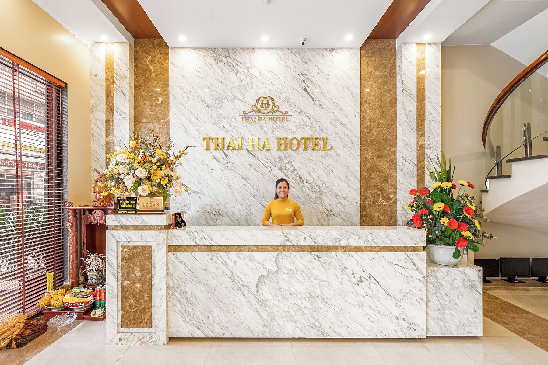 Una recepción de hotel con mostrador de mármol, una recepcionista y arreglos florales.