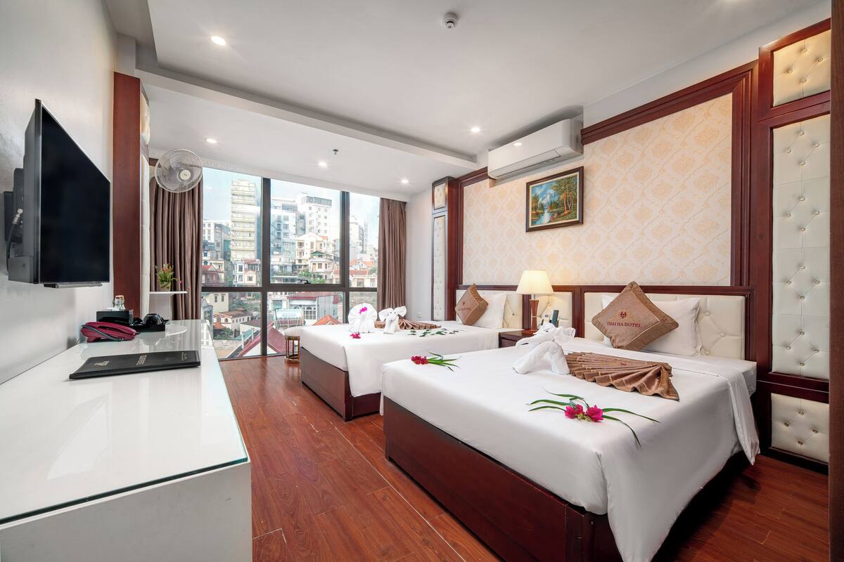 A hotel room with two beds, a desk, a TV, and a city view.
