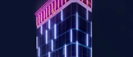 A multi-story hotel with a modern glass facade and neon signage.