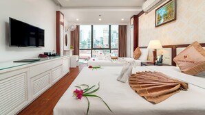 A hotel room with a large bed, a desk with a flat-screen TV, a window with a city view, and a painting on the wall. - Thai Ha Hotel (Bai Chay)